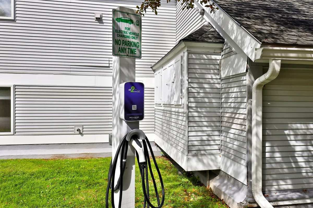 The exterior of the complex featuring an electric vehicle charging station, green signage, and the building’s facade. This modern amenity signals convenience and eco-friendliness, reinforcing the family- and group-oriented atmosphere.