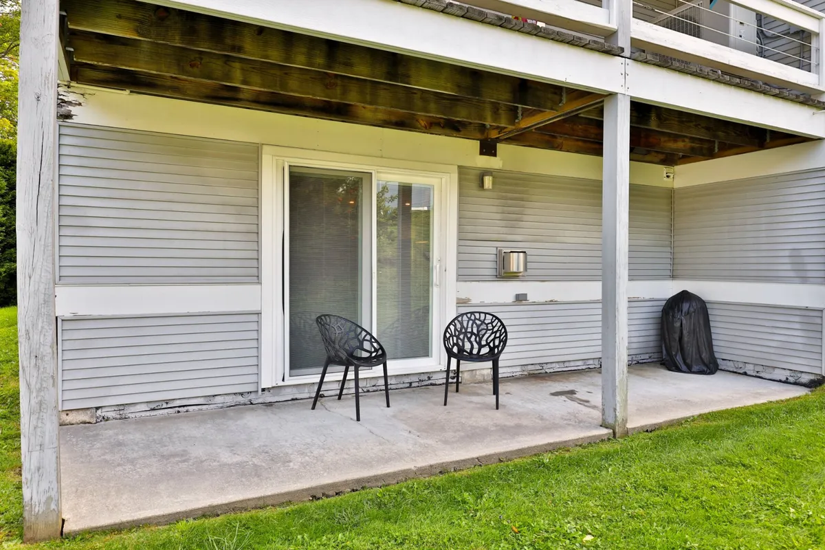 This image presents a peaceful outdoor seating area: two black chairs on a small patio beside a sliding glass door, overlooking a green lawn. The ambiance is calm—ideal for a morning coffee or unwinding after hitting the slopes.
