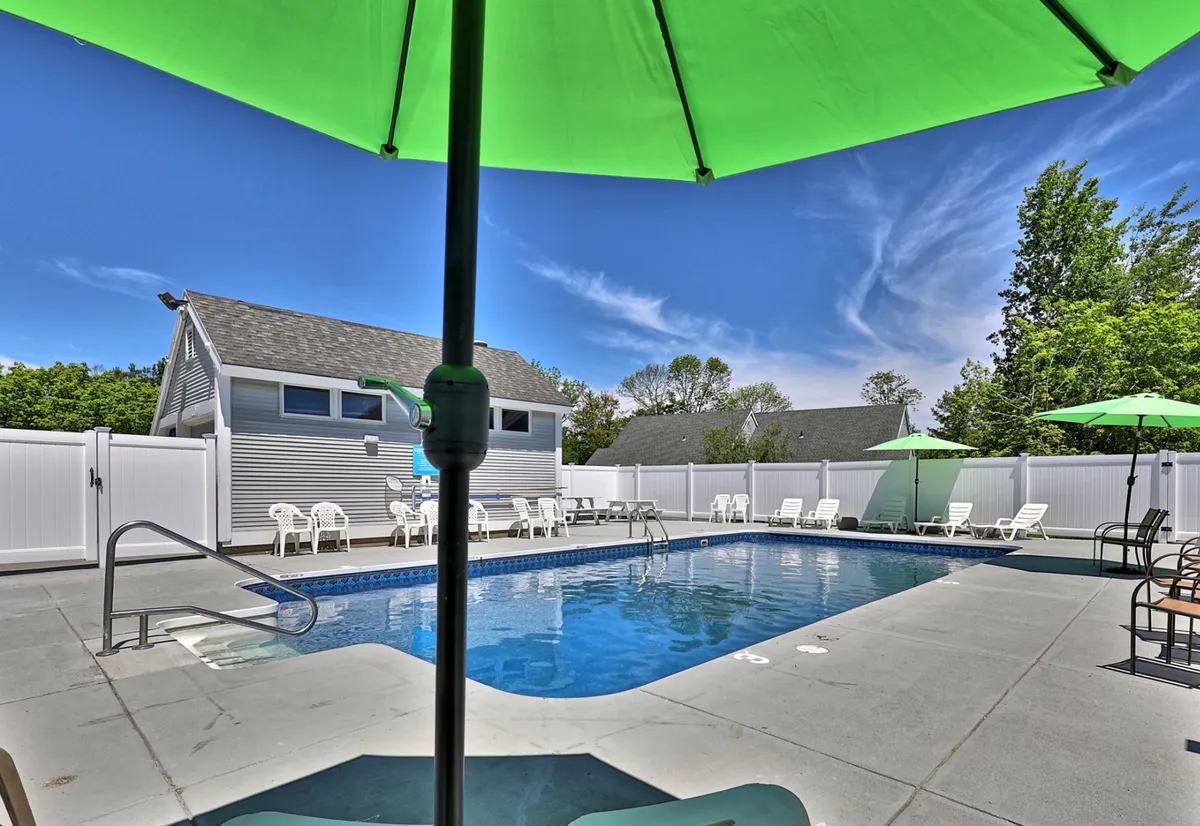 An inviting outdoor heated swimming pool surrounded by lush greenery, bright green umbrellas, and ample seating, ideal for family relaxation or fun under the sun. The building facade of the inn-style complex is visible in the background, reinforcing proximity and access.