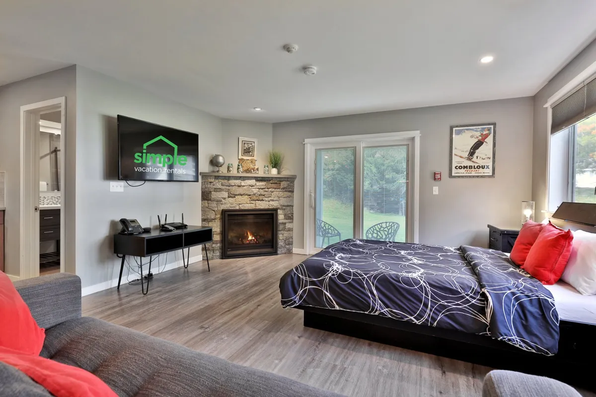 A cozy living space anchored by a gas fireplace, queen bed, and television, with warm lighting that creates an inviting nook for relaxation. The fireplace flickers beside the bed and sofa, making this area perfect for unwinding after a day outdoors.