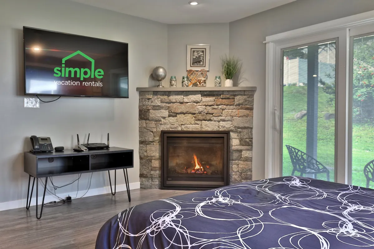 A bedroom area with a fireplace, television, and neatly made bed, accented by decorative items on the mantel. The scene radiates warmth and comfort, inviting guests to relax by the fire or enjoy a quiet evening in.