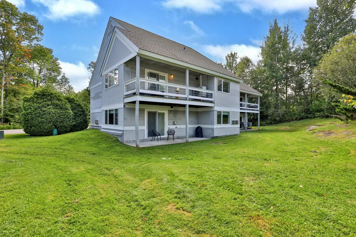 This exterior shot showcases a two-story condo building surrounded by a spacious green lawn. Balconies provide outdoor relaxation spots, while the open area in front allows for gatherings, play, or gear preparation.