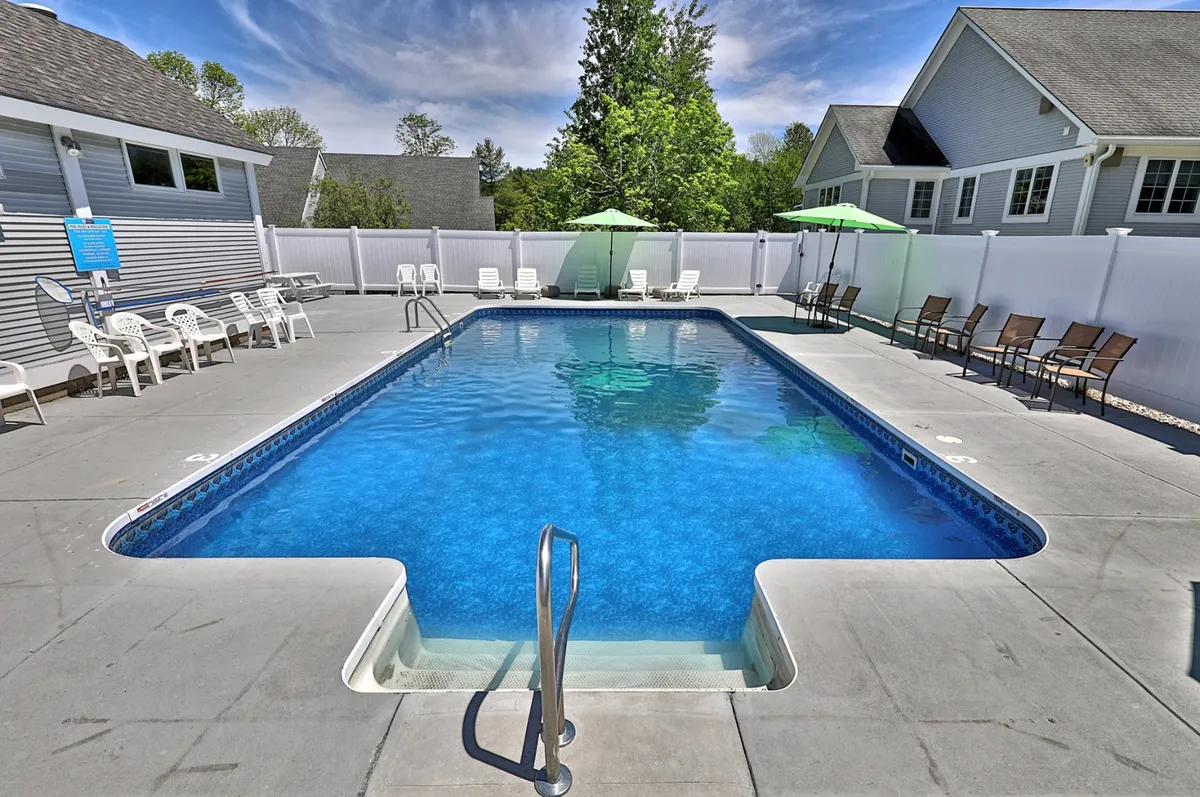 A close-up view of the pool area, featuring sparkling blue water, surrounding greenery, comfortable lounge chairs, and large umbrellas. The scene conveys a sense of leisure and sociability, with the pool as the central attraction for guests seeking relaxation or fun.