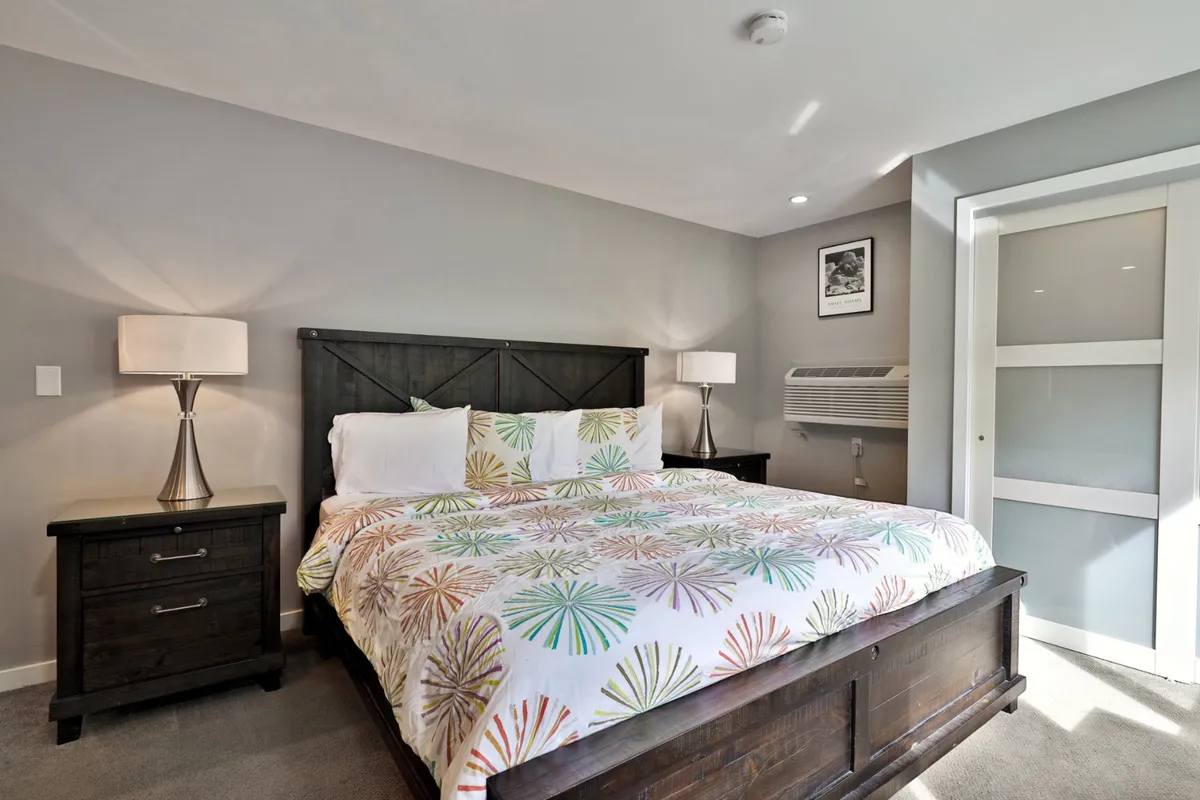 The inviting bedroom displays a bed with vibrant bedding, nightstands with lamps for reading, and tasteful wall art. The mood is warm and welcoming, emphasizing the room’s restful and rejuvenating qualities.