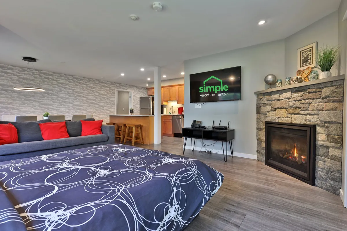 A warm, inviting living area featuring a comfortable sofa with red accents, a TV displaying branding, and a central gas fireplace as the focal point. The space is ideal for both relaxation and social gatherings, and showcases the cozy ambiance that the gas fireplace provides year-round.